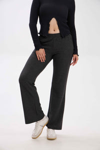 Person wearing black long-sleeve top and dark gray flared pants on a white background.