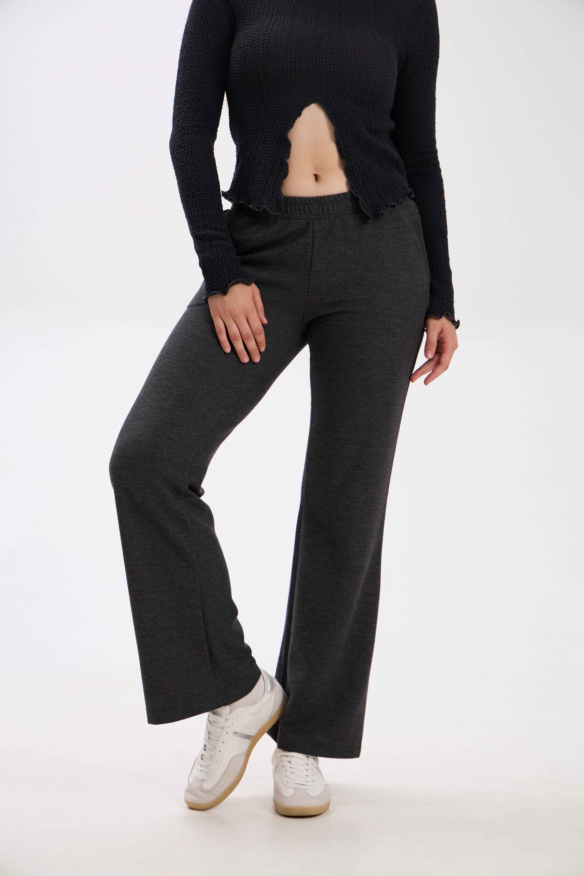 Person wearing black long-sleeve top and dark gray flared pants on a white background.