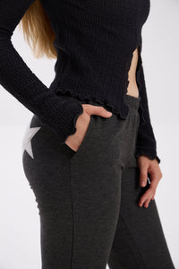 Person wearing a black long-sleeve top and gray pants on a white background.