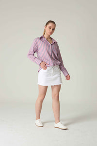 Woman wearing a pink striped shirt and white shorts on a plain background.