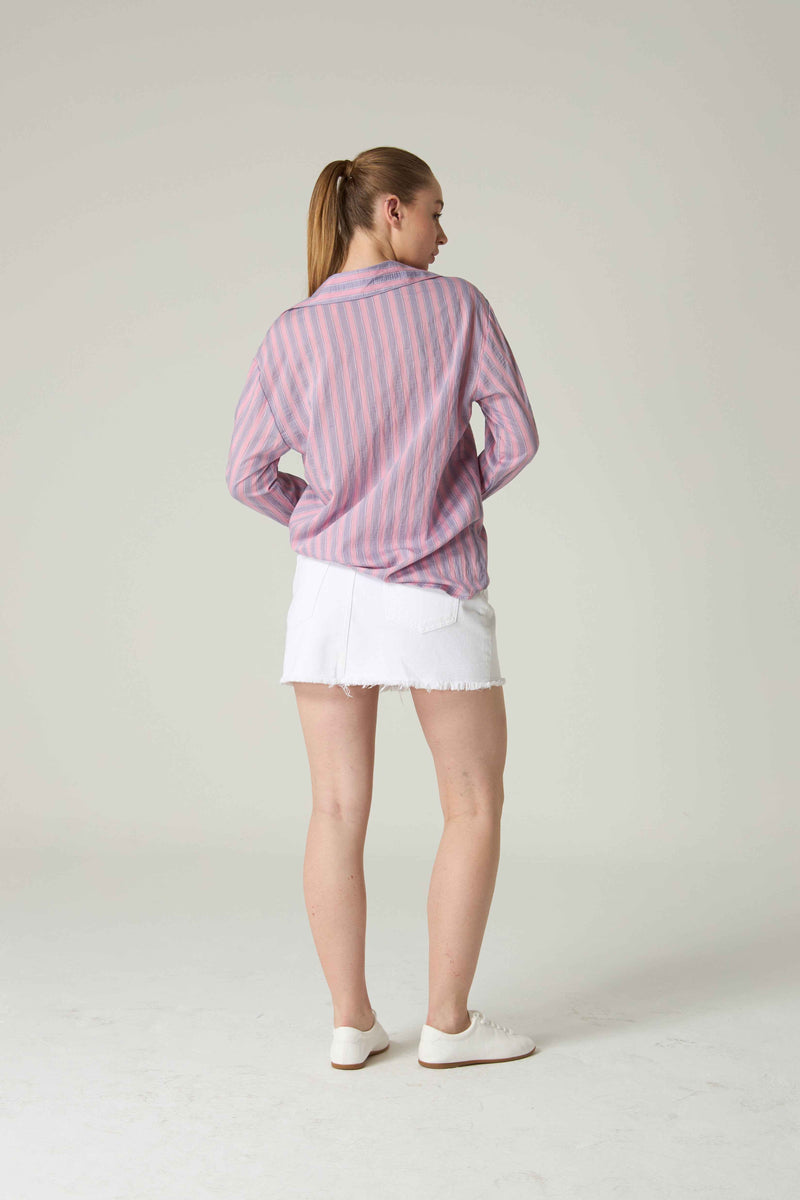 Person wearing a pink and white striped shirt with a white skirt on a plain background.