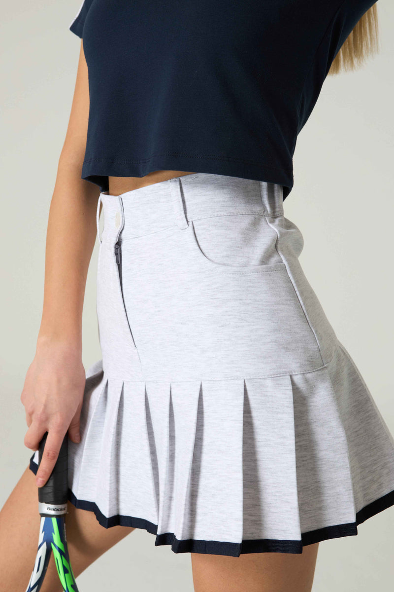 Person wearing a gray tennis skirt with a black top against a neutral background.