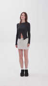 Person wearing a fitted black long-sleeve top with a front slit, paired with a light grey mini skirt, white socks, and black shoes.