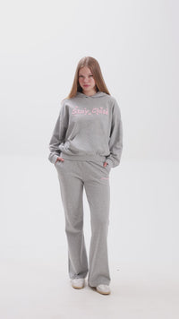 Person wearing grey melange sweatpants and matching hoodie with pink “Stay Close” embroidery.
