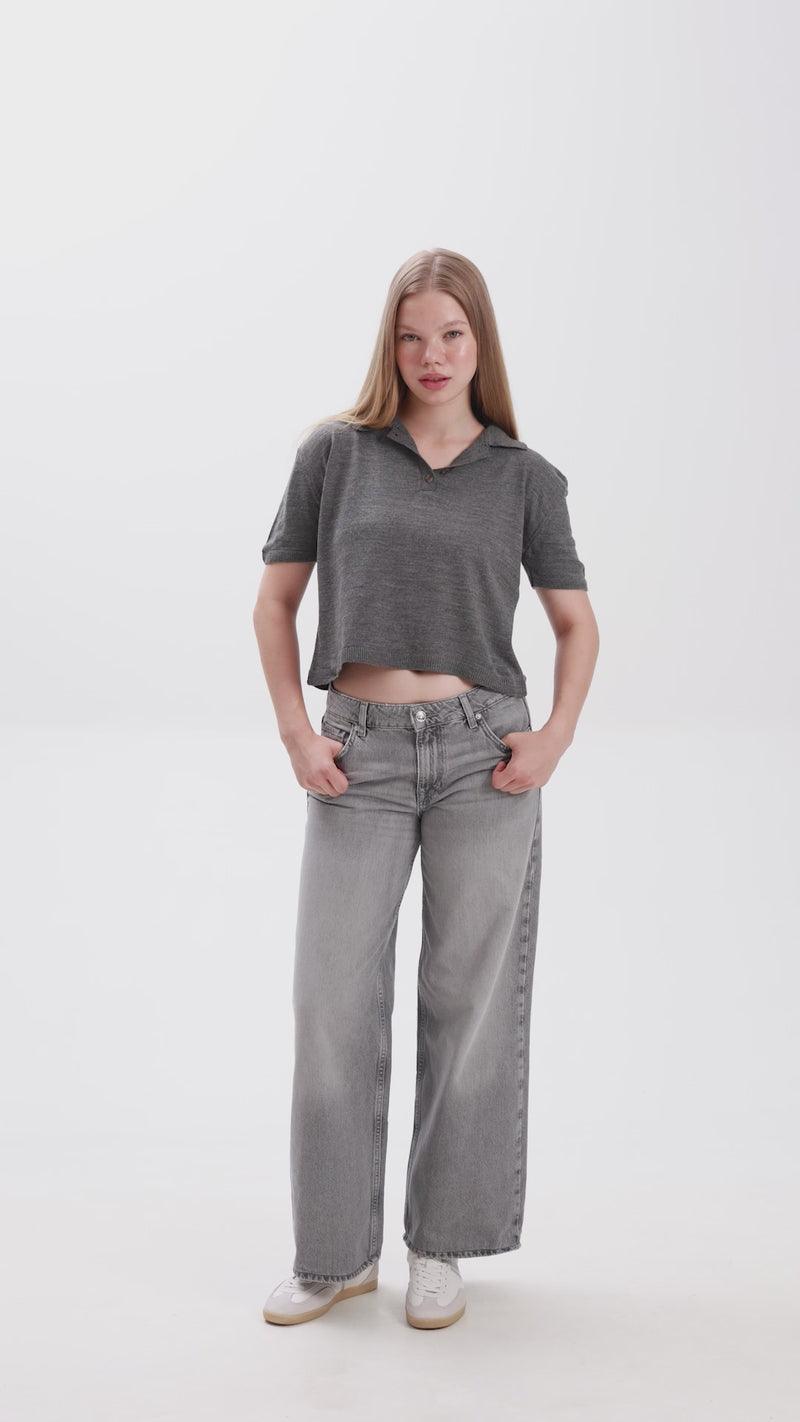Person wearing a gray cropped polo shirt and gray jeans on a white background