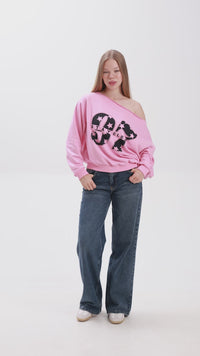 Model showcasing a pink off-shoulder sweatshirt with bold “Stay Close” print, paired with blue jeans and white sneakers.