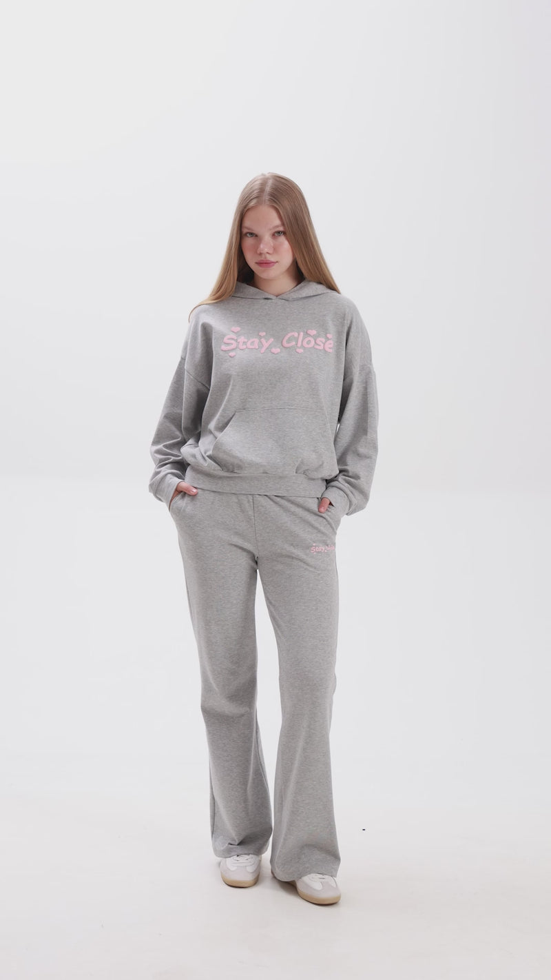 Grey hoodie and sweatpants set with pink Stay Close logo, elastic waistband and relaxed fit for everyday comfort.