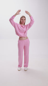 Model dancing in a pink Stay Close loungewear set, featuring a cropped sweatshirt and straight-fit sweatpants with white sneakers.