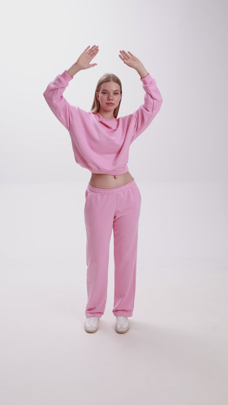 Model dancing in a pink Stay Close loungewear set, featuring a cropped sweatshirt and straight-fit sweatpants with white sneakers.