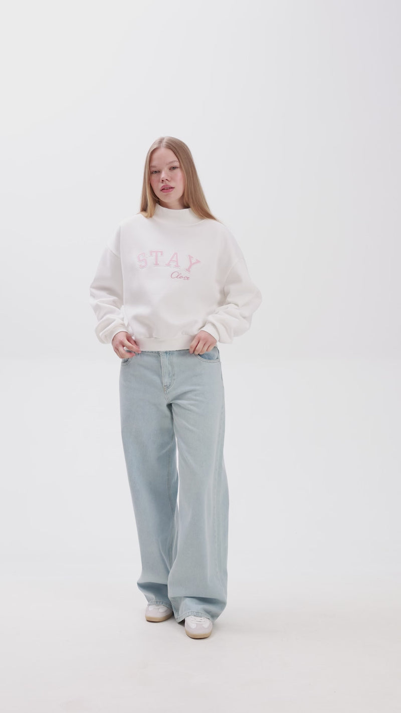 Person wearing white sweatshirt with pink text showcasing her clothing, on a plain background